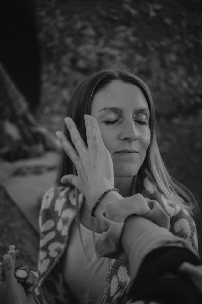 Schwarz-Weiß-Porträt einer Frau mit geschlossenen Augen, während eine Hand sanft Glitzer auf ihr Gesicht malt. Ausdruck von Hingabe, Transformation und innerem Leuchten