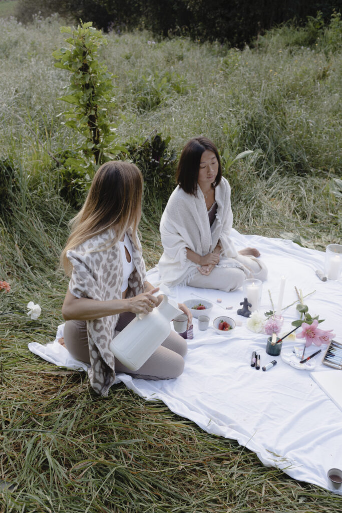 Frau sitzt in weichem Licht mit geschlossenen Augen und Hand auf dem Herzen, während sie ein Ritual zur Verbindung mit ihrem Zyklus und ihrer inneren Ruhe praktiziert.