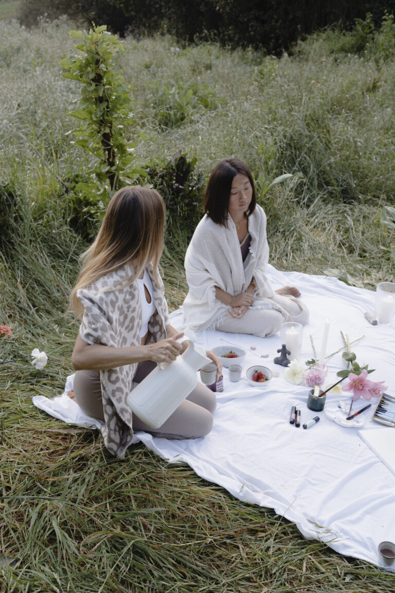 Frau sitzt in weichem Licht mit geschlossenen Augen und Hand auf dem Herzen, während sie ein Ritual zur Verbindung mit ihrem Zyklus und ihrer inneren Ruhe praktiziert.