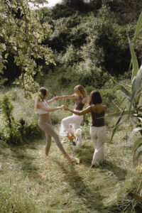 Frau sitzt in weichem Licht mit geschlossenen Augen und Hand auf dem Herzen, während sie ein Ritual zur Verbindung mit ihrem Zyklus und ihrer inneren Ruhe praktiziert.