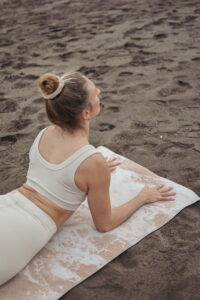 Alena praktiziert Yoga am Strand, barfuß auf sandigem Boden, mit geöffnetem Herzraum und weitem Blick aufs Meer, während die Morgenluft sie umgibt. Das Bild strahlt Ruhe, Erdung und Verbindung aus und lädt ein, Yoga als Rückkehr in den Körper und ins Leben zu erleben.